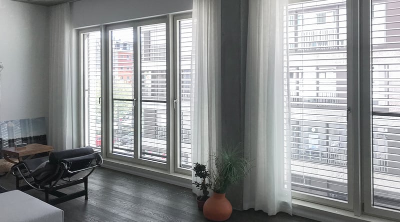 Heller Raum mit weißen Stores vor Balkontür und Fensterfront