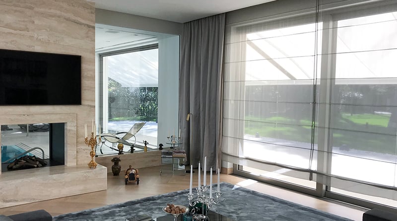 Grauer Vorhang neben einem raumhohen Fenster mit Rollo in einem Wohnzimmer mit Kamin