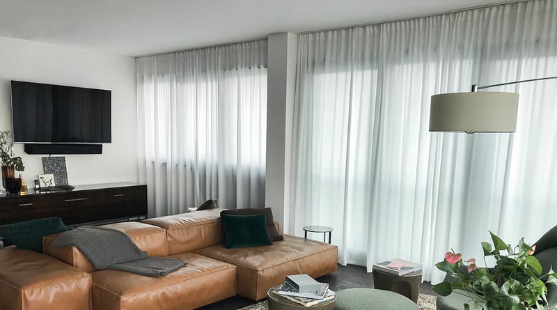 Wohnzimmer mit Ledersofa, grauen Vorhängen und weißem Store vor der Fensterfront