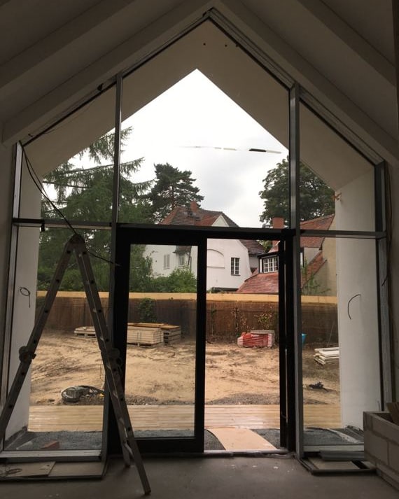 Großes Giebelfenster über zwei Geschosse im Rohbau, ohne Vorhänge, draußen eine Baustelle